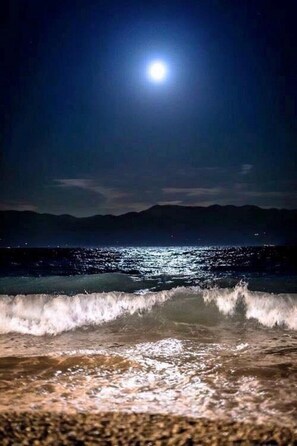 A nighttime beach scene with waves approaching the shore and a bright moon in the sky.