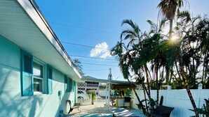 Ein Haus mit einer Terrasse, komplett mit Tisch und Bänken, umgeben von einem weißen Zaun und Palmen.