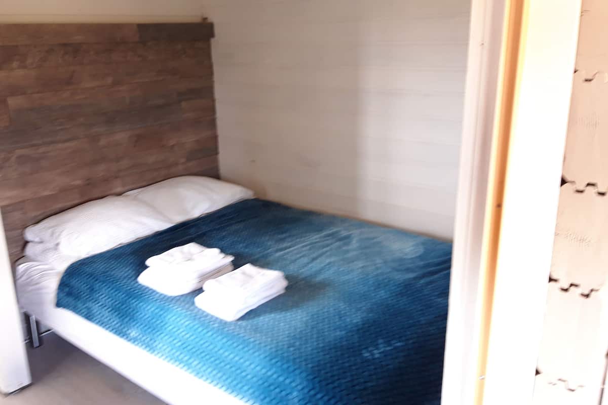A small, single-bed room with a wooden headboard, a blue bedspread, and two white towels on the bed.