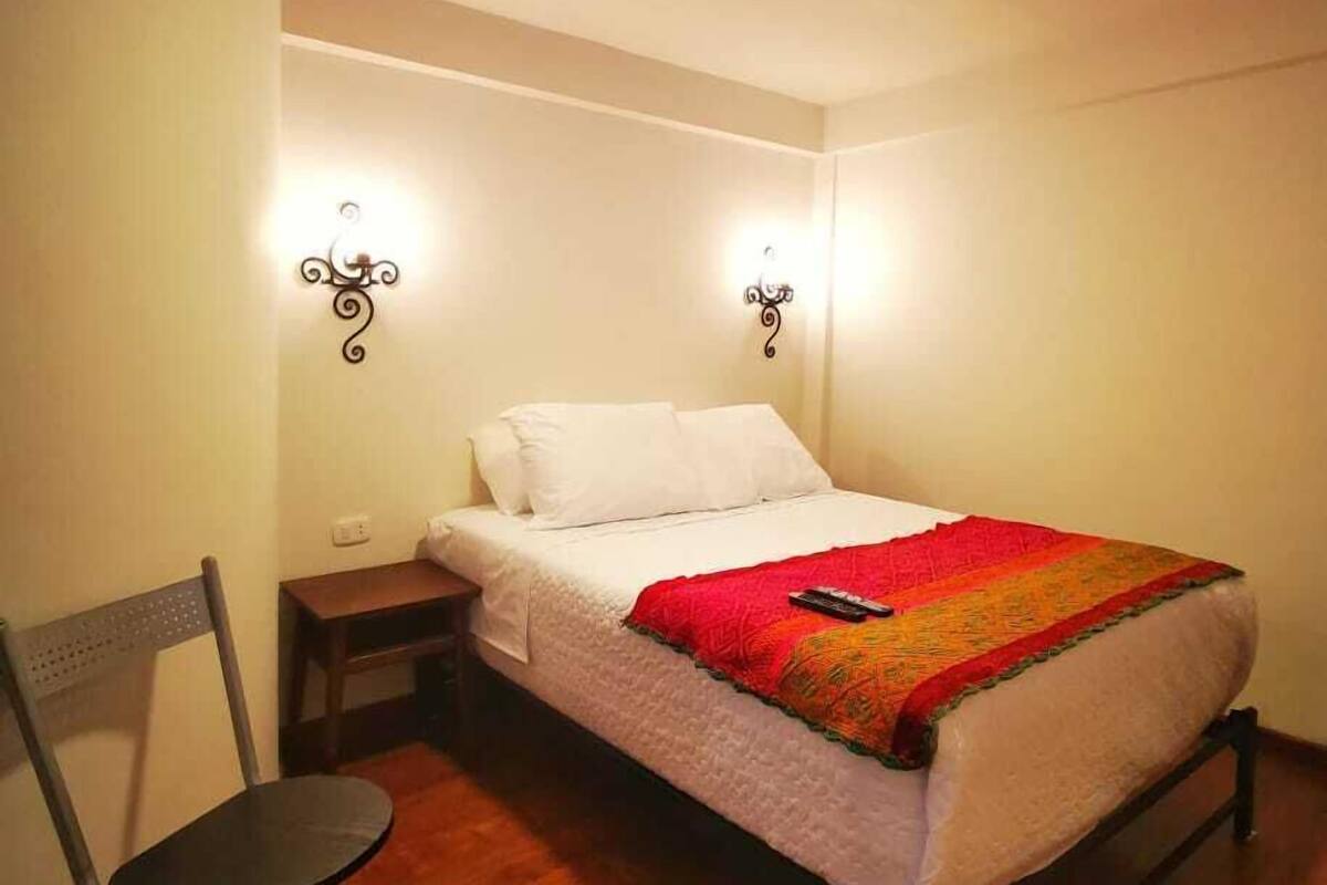 A small, cozy bedroom with a single bed, a chair, and two wall-mounted lamps.
