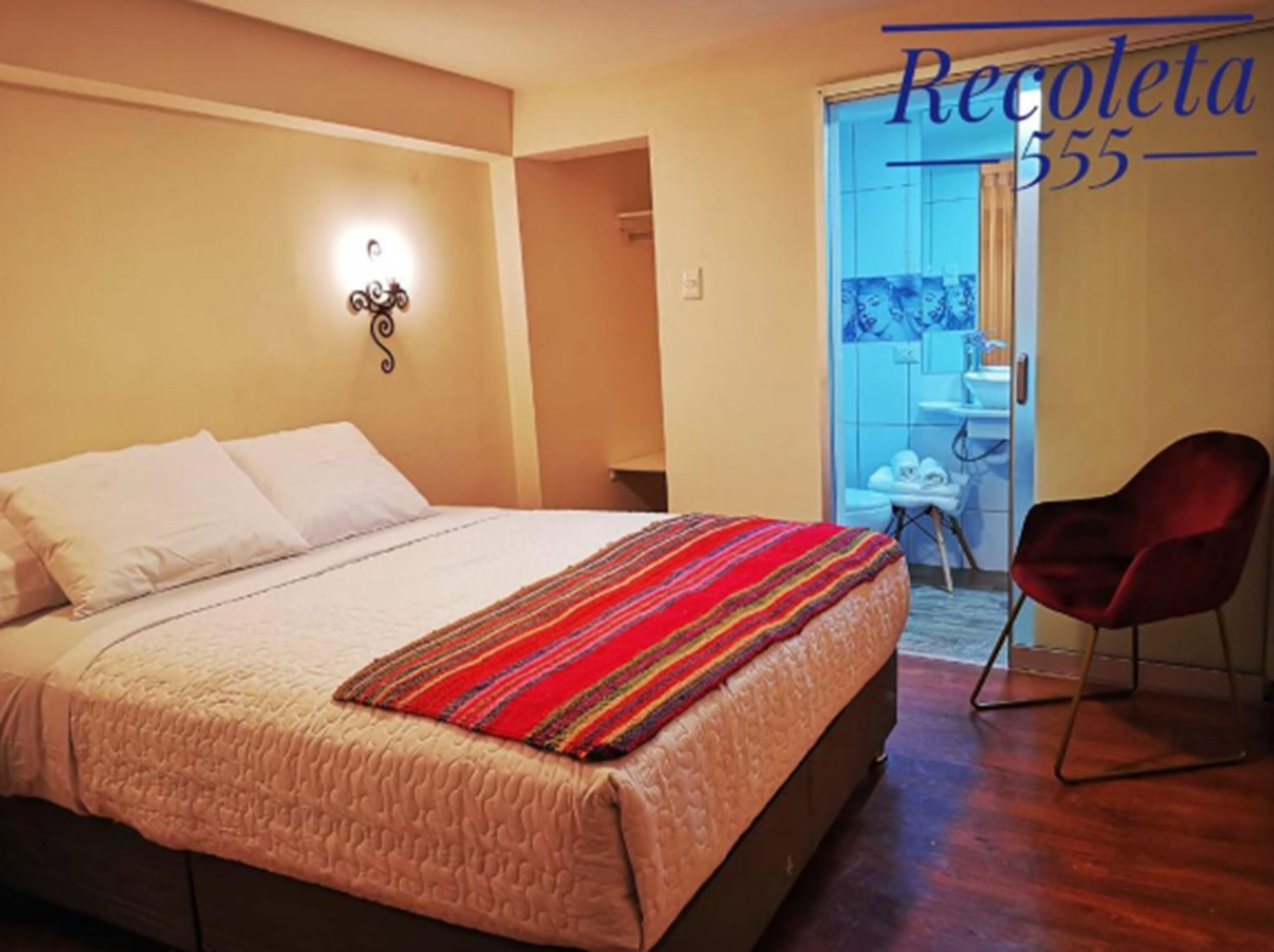 A bedroom with a bed, a red chair, and a bathroom visible through an open door.