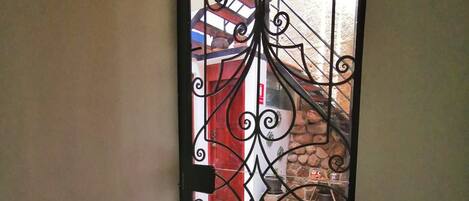 Una reja metálica con diseños intrincados, que conduce a una escalera con una puerta roja y un muro de piedra.