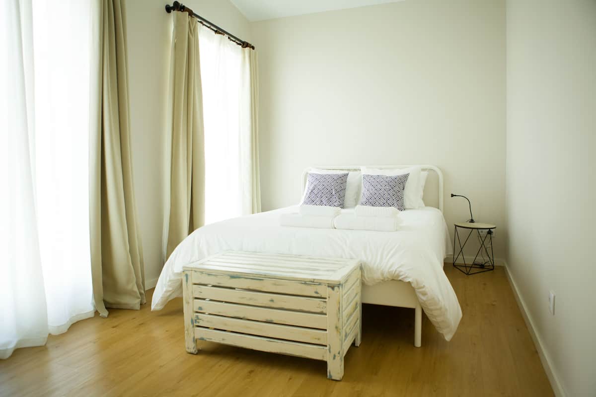 A bedroom with a bed, a bedside table, a lamp, and a window with curtains.
