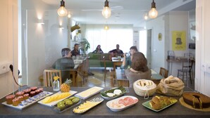 Ein Essbereich mit einem Buffet, das verschiedene Speisen anbietet, sowie eine Gruppe von Personen, die im Hintergrund an einem Tisch sitzen.
