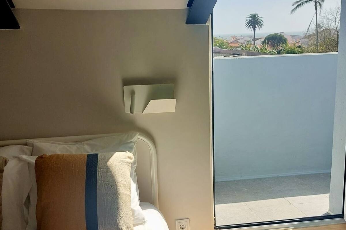 A bedroom with a large bed, a window with a view of palm trees, and a wooden floor.