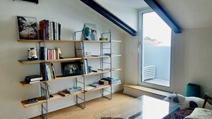 Ein modernes Wohnzimmer mit einem Glastisch, Holzboden und einem Bücherregal voller Bücher und Dekoration.
