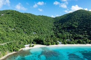 A tropical beach with clear turquoise waters, surrounded by dense green forest and hills. - Kallaloo: Walk to Gibney Beach! (St. John)