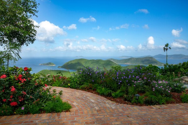 A landscaped garden with a brick pathway, lush greenery, and vibrant flowers.