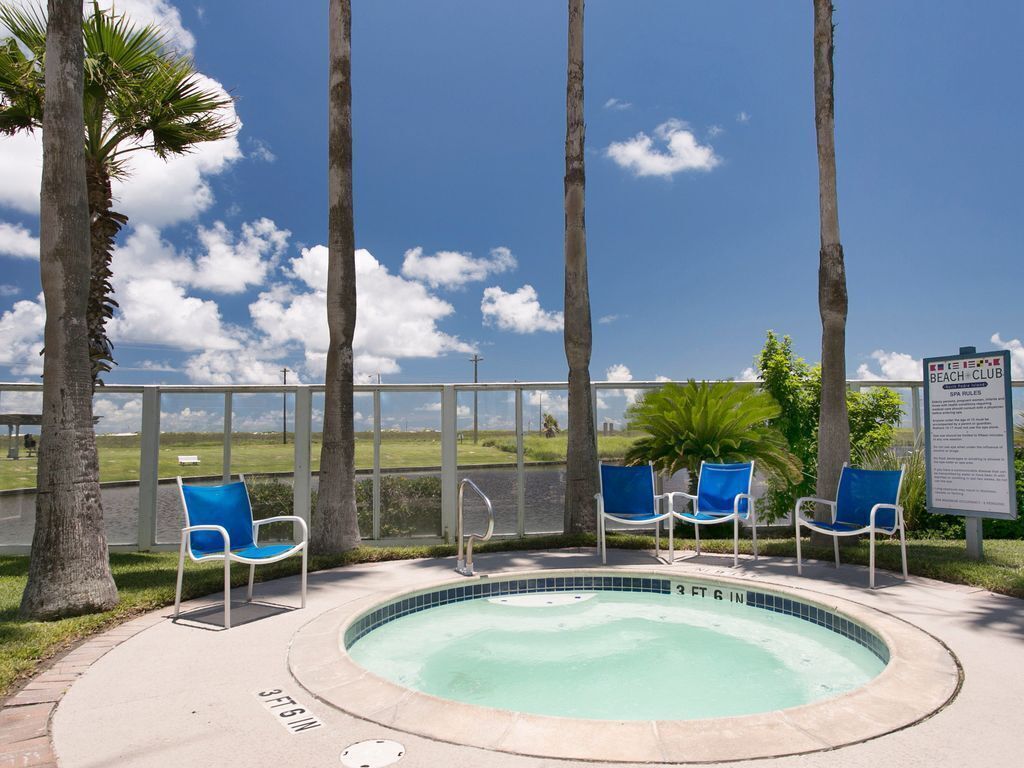 A pool area with a 3 FT deep sign, surrounded by palm trees and chairs, with a beach club sign in the background.