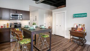 Una cocina moderna con armarios oscuros, electrodomésticos de acero inoxidable y una mesa de comedor de madera con taburetes de bar. Un cartel en la pared dice "Greenspan".