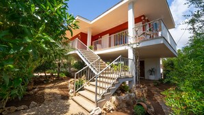 A two-story house with a balcony, a staircase, and a garden with various plants and rocks. - Sa Marina by dracmallorca (Cala Santanyi)