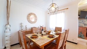 A dining area with a wooden table set for four, surrounded by chairs. A round mirror hangs on the wall, and a unique hexagonal light fixture is above the table. - Sa Marina by dracmallorca (Cala Santanyi)