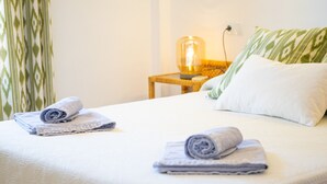 A neatly made bed with two rolled towels, a green and white striped pillow, and a small wooden nightstand with a lamp. - Sa Marina by dracmallorca (Cala Santanyi)