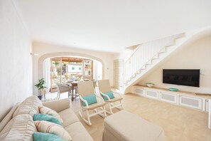 Ein großzügiger Wohnbereich mit einer Couch, Sesseln, einem Fernseher und einer Treppe.