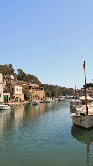 A marina with boats docked, buildings along the shore, and a clear sky.