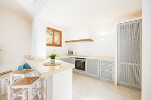 Cocina moderna con una isla central, horno empotrado, microondas y estante de madera colgante.