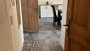 Un couloir avec des carreaux de sol à motifs, une porte en bois, un bureau avec une chaise et un tableau encadré au mur.