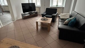 Un salon avec un téléviseur, un canapé, une table basse et une table en bois.