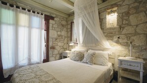Un dormitori amb una paret de pedra, un llit amb dosser, roba de llit blanca i taules de nit amb làmpades.
