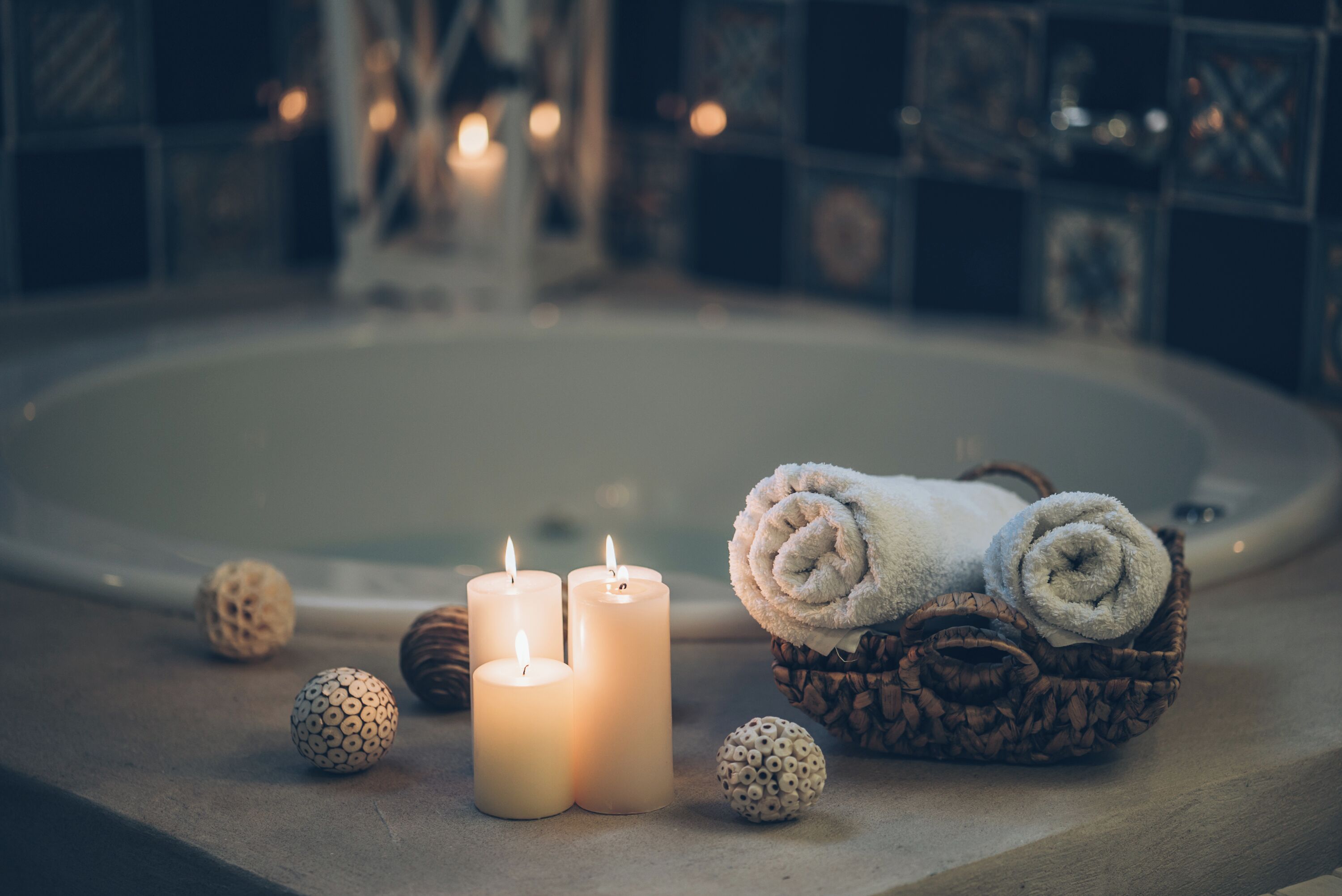 A bathroom with three lit candles, a basket of rolled towels, and decorative spheres on a countertop.