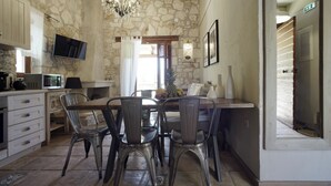 Cuina amb parets de pedra, un lampadari, taula de menjador amb cadires, televisor i microones.