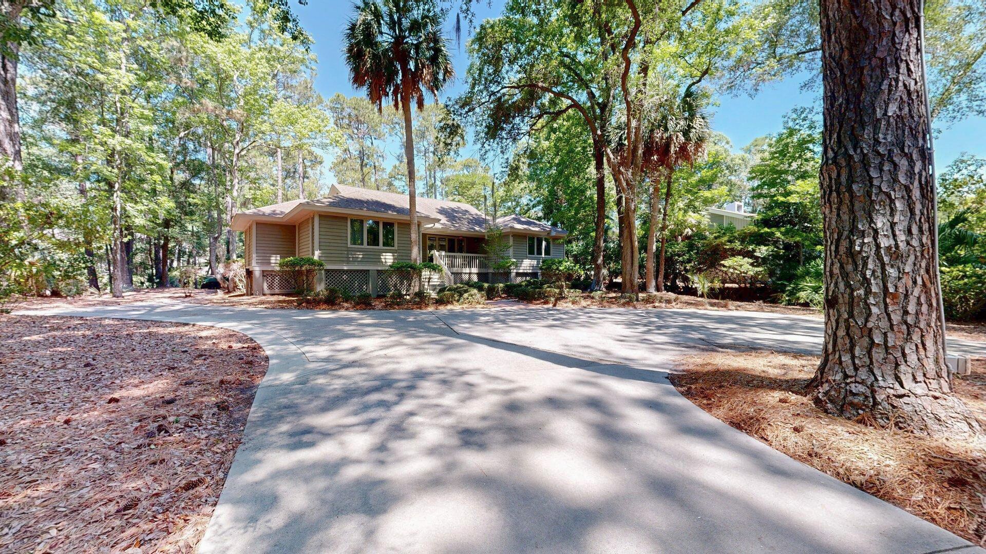 A single-story house with a front porch, surrounded by trees and a driveway.