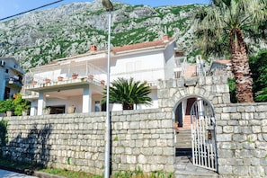 A stone wall with a gate, a white building with a balcony, and a mountain in the background. - Waterfront Apartment Petrovina (Kotor)