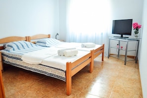 A neatly made bed with a patterned bedspread, a wooden headboard, and two rolled towels. There is a television on a glass table beside the bed. - Waterfront Apartment Petrovina (Kotor)