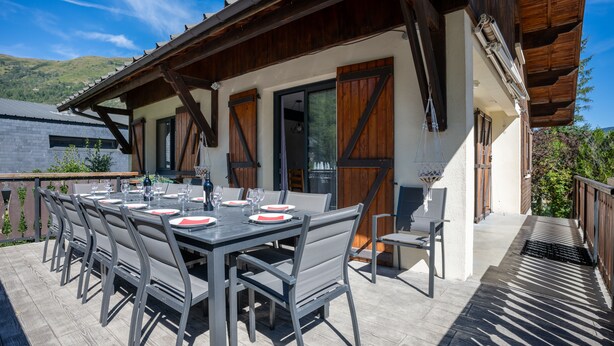 Ein Essbereich im Freien mit einer Holzpergola, einem Tisch gedeckt mit Tellern und Gläsern, und Blick auf die umliegende Landschaft.