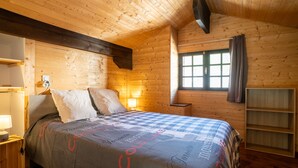 Ein gemütliches Holzhütten-Zimmer mit Bett, Nachttisch, Lampe und einem Vorhangfenster.