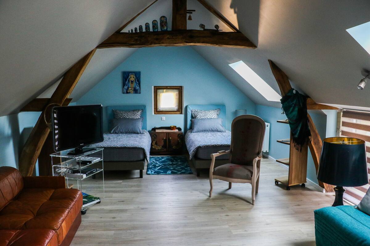 A cozy attic bedroom with two beds, a TV, a wooden chair, and a desk.