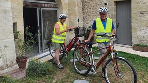 Two people in safety vests standing next to bicycles in front of a stone building with an arched entrance and a door. - Les Voies Blanches (Vouvray)