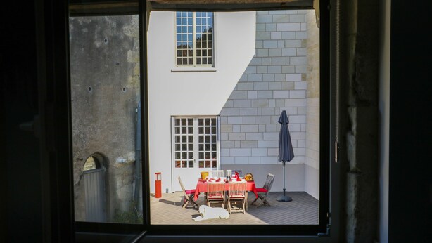 A room with a sliding glass door leading to an outdoor patio area with a table and chairs. - Les Voies Blanches (Vouvray)