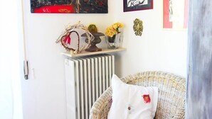 Une pièce avec un fauteuil en osier, un radiateur et des œuvres d’art accrochées au mur.