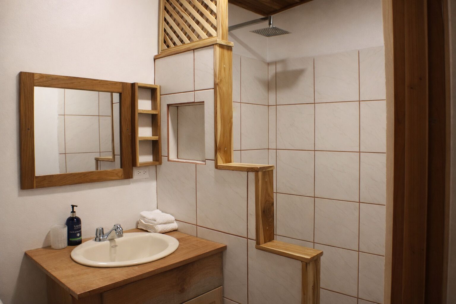 Un bagno con un mobile vanitario in legno, un lavandino, uno specchio e una zona doccia.