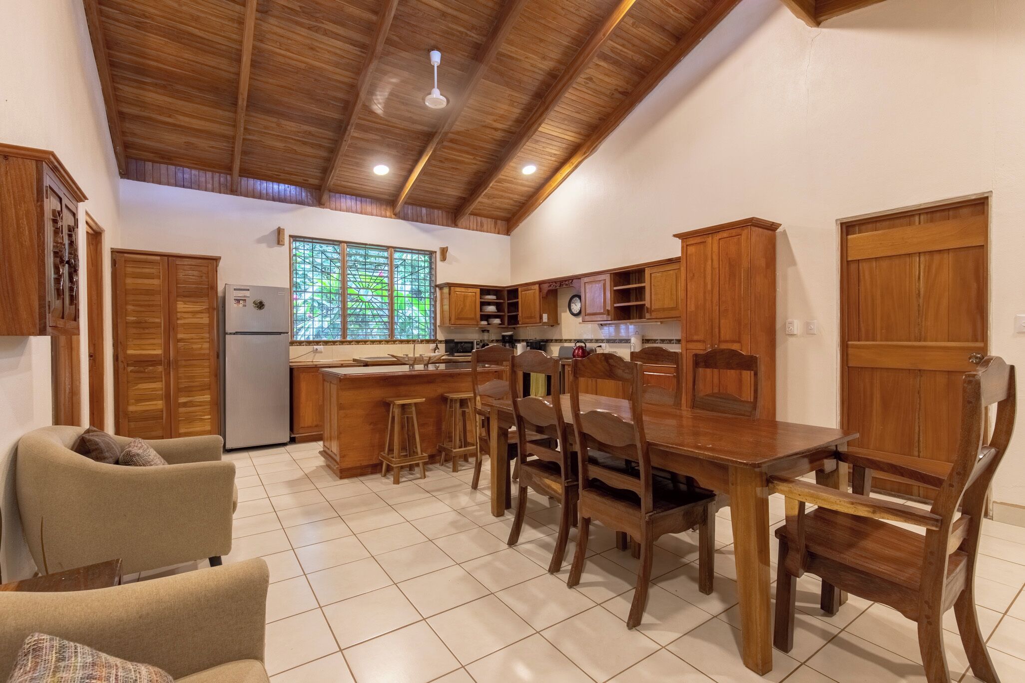 Une cuisine avec des meubles en bois, un réfrigérateur et un coin repas comprenant une table et des chaises.