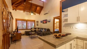 Amplia sala de estar con techo alto, un sofá, una mesa de centro y una cocina con armarios blancos.