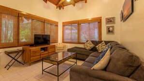 Una sala de estar con televisión, sofá, mesa de centro y vigas de madera en el techo.