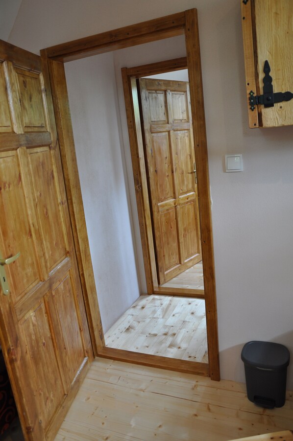 Puerta de madera que da a una habitación con suelo de madera y un cesto negro.