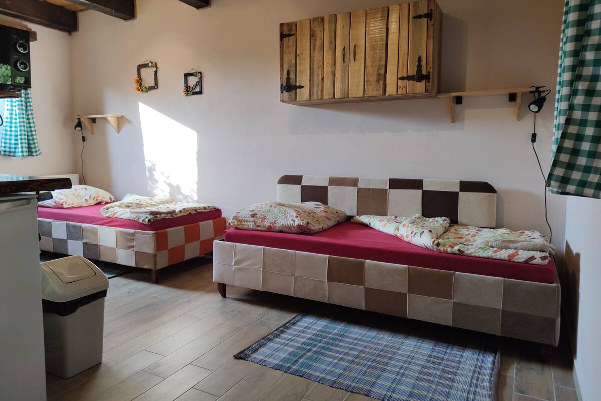 Een kamer met twee bedden, houten balken in het plafond, een klein raam en een wandplank.
