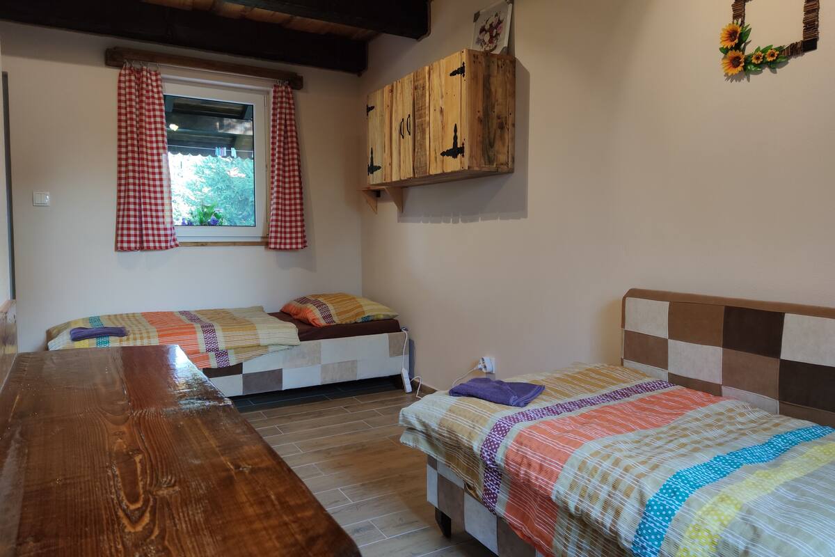 Een kamer met twee bedden, een houten tafel, een raam met geruit gordijn en een houten kast.