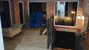 A spacious living area with a blue armchair, a patterned sofa, and a staircase with a black railing. - András pension (Krasnohorske Podhradie)
