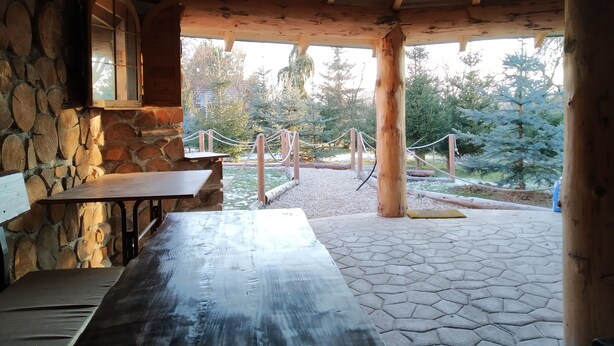 A covered outdoor area with stone walls, wooden benches, and a view of trees and a pathway. - András pension (Krasnohorske Podhradie)
