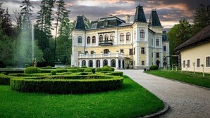 A large, historic building with multiple towers and a formal garden. - András pension (Krasnohorske Podhradie)