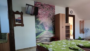 A bedroom with a bed, a TV mounted on the wall, a large floral artwork, a wooden wardrobe, and a door leading to another room. - András pension (Krasnohorske Podhradie)