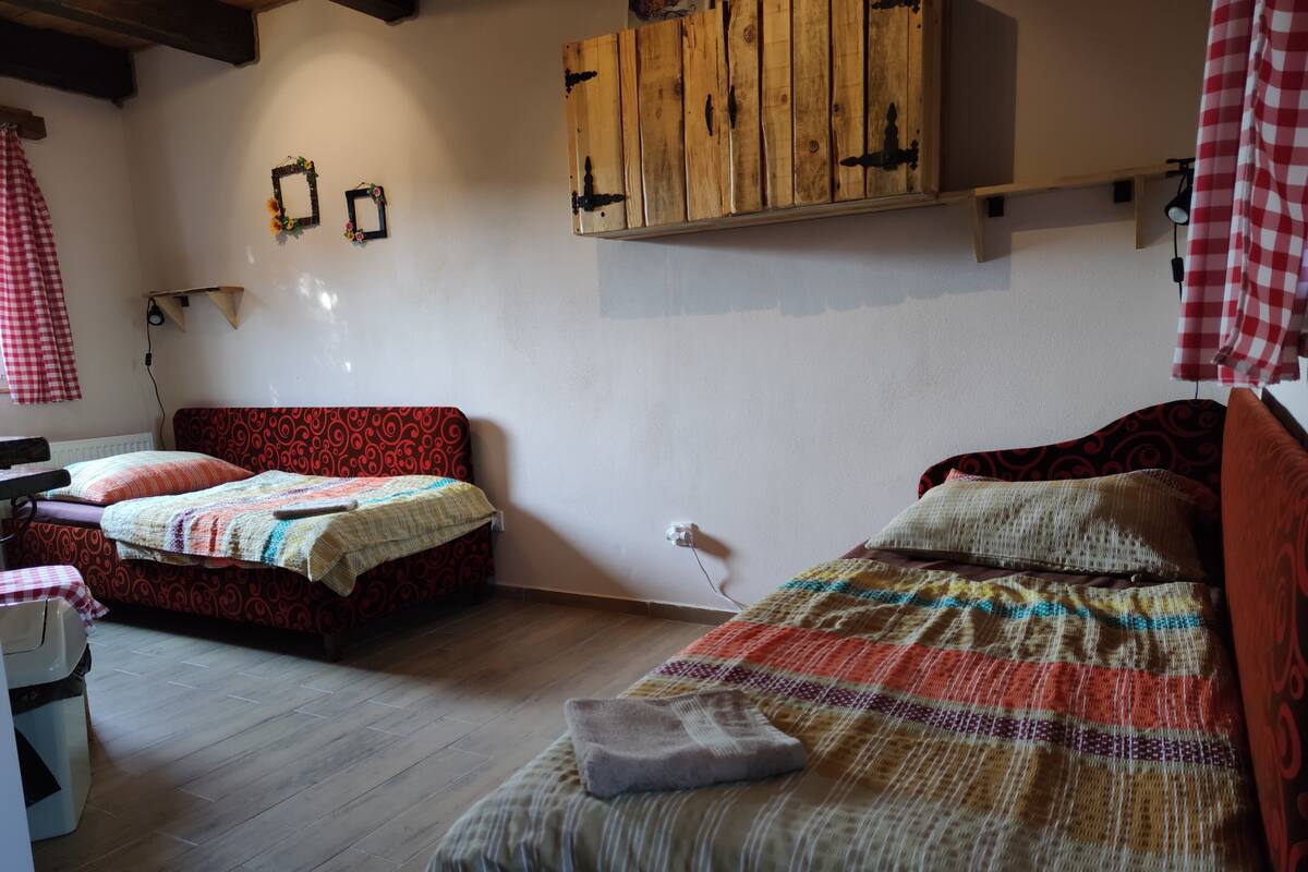 Een slaapkamer met twee bedden, houten balken in het plafond, een klein tafeltje en een wandplank.