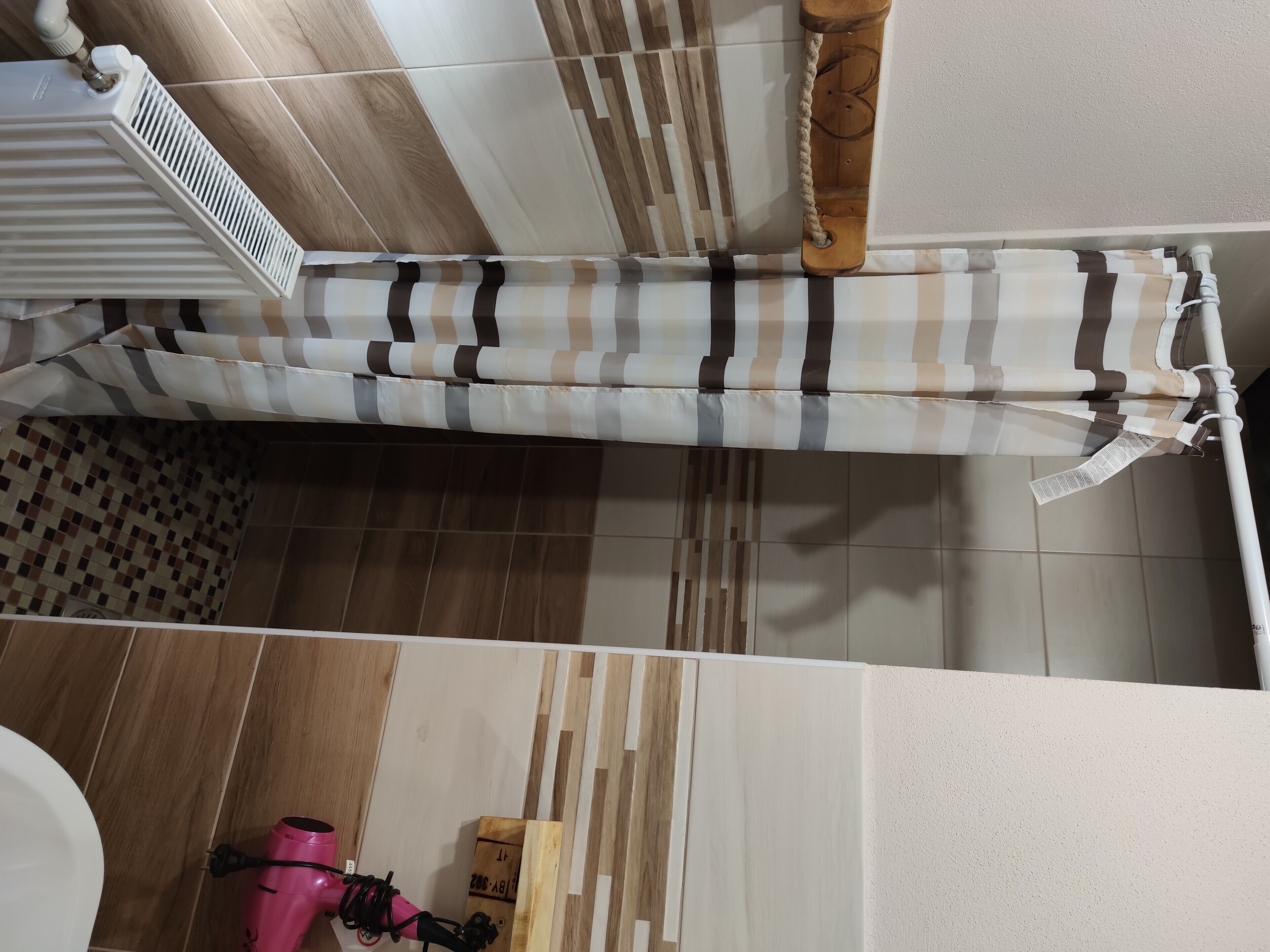 Un baño con cortina de ducha a rayas, un radiador blanco y un secador de pelo rosa.