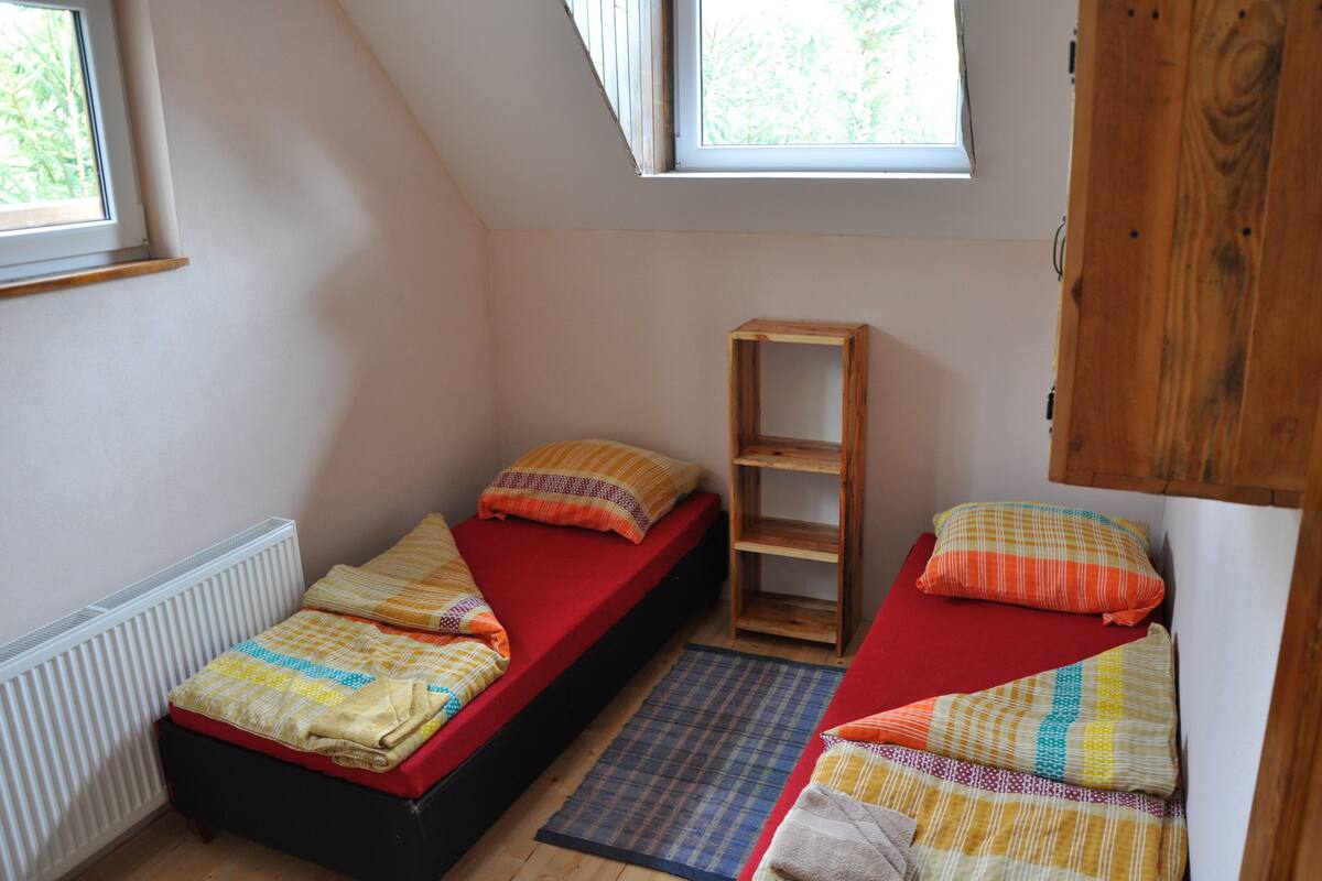 Een kleine kamer met twee enkele bedden, een houten plank en een radiator.