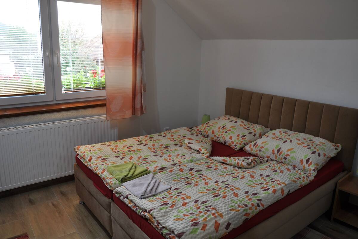Een slaapkamer met een bed, een raam met zonwering, een radiator en een gordijn.