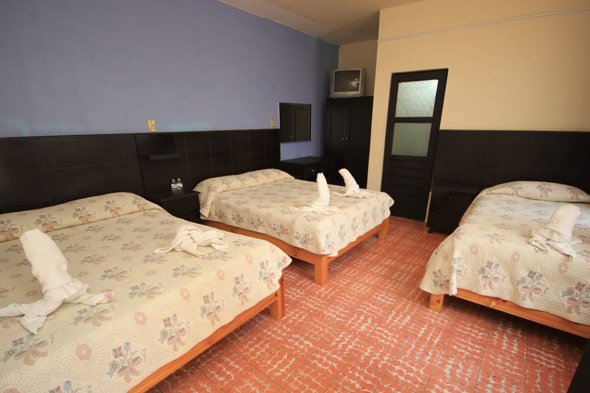 Una habitación de hotel con tres camas, un televisor sobre un mueble bajo y un espejo en la pared.